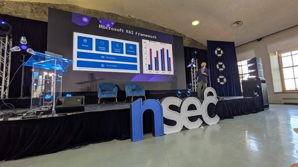 Photograph taken at an angle of the nsec conference stage where a speaker is looking at the projector screen